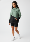 Woman wearing a green and black two-tone hoodie with black shorts on a white background